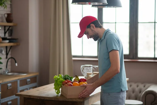 Чоловік у червоному капелюсі кладе коробку з продуктами на стіл — стокове фото