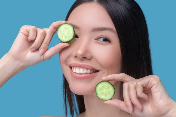 Sorrindo bonito jovem segurandofatias de pepino e sentimento apreciado — Fotografia de Stock