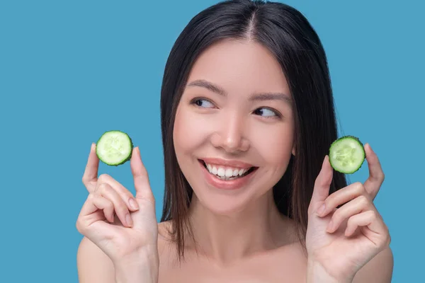 Sorrindo bonito jovem segurandofatias de pepino — Fotografia de Stock