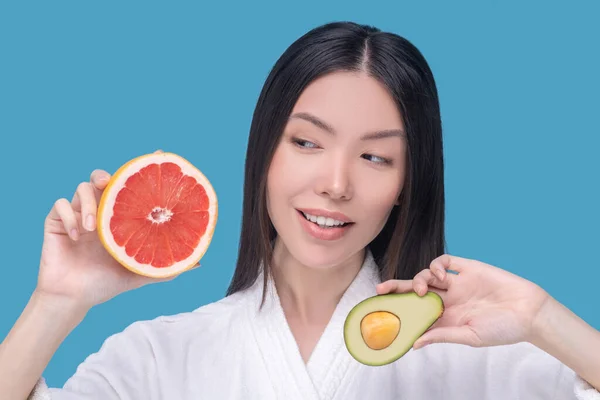 Ung asiatisk kvinna som håller en halv avokado och skiva grapefrukt — Stockfoto