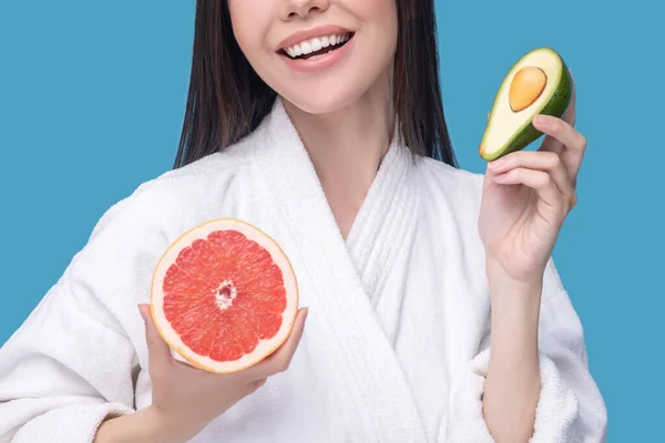 Leende ung kvinna som håller en halv avokado och skiva grapefrukt — Stockfoto