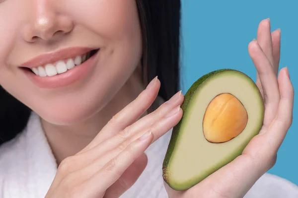 Joven sonriente sosteniendo la mitad del aguacate — Foto de Stock