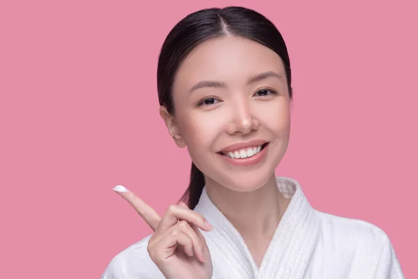 Bastante asiático chica sonriendo y mostrando crema en su dedo — Foto de Stock