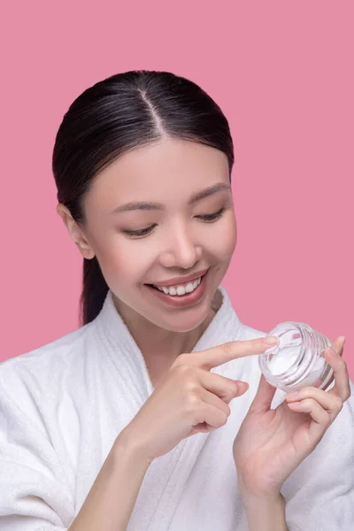 Досить азіатська дівчина бере крем з баночки і посміхається — стокове фото
