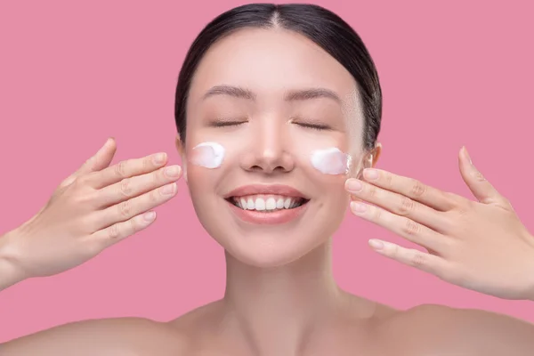Gadis asia cantik yang mengoleskan krim di wajahnya — Stok Foto