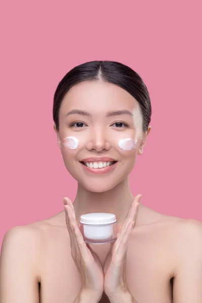 Досить азіатська дівчина тримає банку крем для обличчя і посміхається — стокове фото