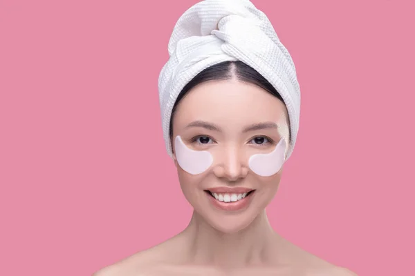Lächelnde Asiatin mit weißem Kopftuch und Augenklappen fühlt sich wohl — Stockfoto