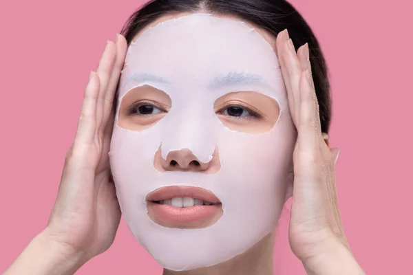 Dark-haired asian girl applying moisturizing mask on her face — Stock Photo, Image