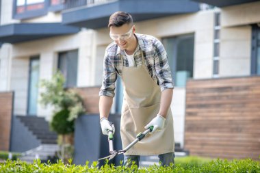 Koruyucu gözlüklü koyu saçlı erkek dışarıda çalıları buduyor.