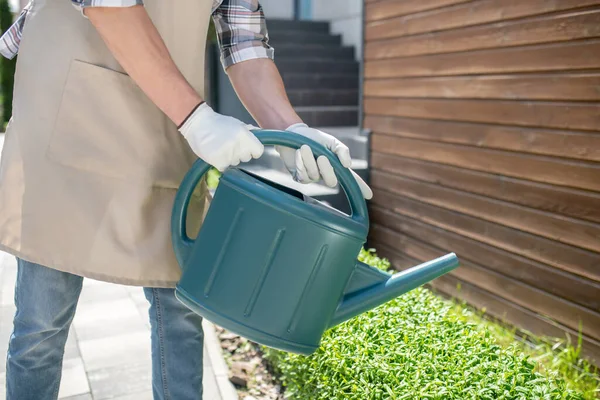 Close-up of male hands in protective gloves watering bushes with watering can in the yard — Stock Photo, Image