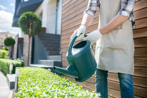 Close-up of male hands in protective gloves watering bushes with green watering can in the yard — Stock Photo, Image