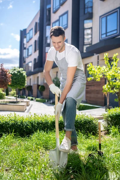 Alegre macho moreno con guantes protectores y delantal cavando con pala — Foto de Stock