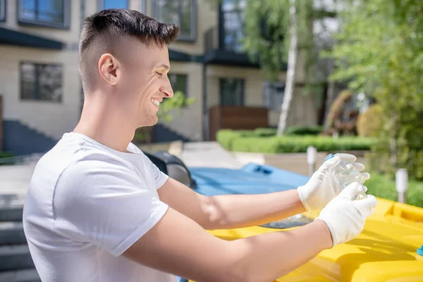 Siyah saçlı, koruyucu eldivenli, plastik şişe sıkan bir erkek.