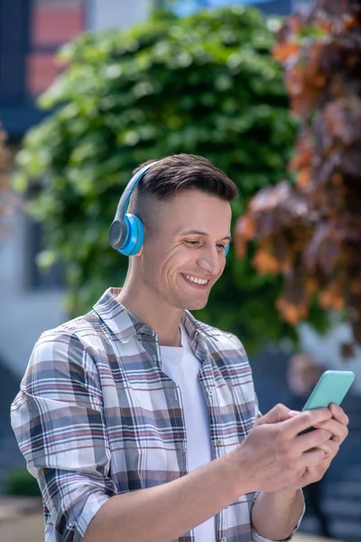 Sorrindo macho de cabelos escuros usando fones de ouvido, conversando ao telefone — Fotografia de Stock
