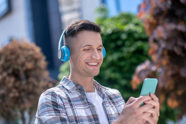 Neşeli koyu saçlı erkek kulaklık takıyor, telefonda sohbet ediyor.