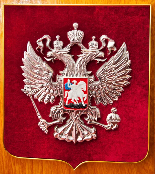 The coat of arms of Russia the image of a two-headed eagle is covered with silver paint on bright red velvet. Symbols of the state of tradition.