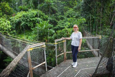 Amazon ormanındaki ağaçlar arasında yüksek irtifada, platformda duran bir kadınla birlikte askıya alınmış yürüyüş yolları. Dünya turizmi, gezi, eko-turizm.