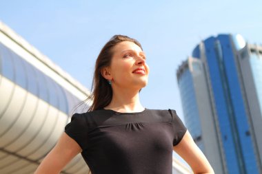 Güneşli bir günde modern ofis binalarının arka planında gökyüzüne bakan genç ve güzel bir iş kadınının portresi. İnsanlar, iş, güzellik..