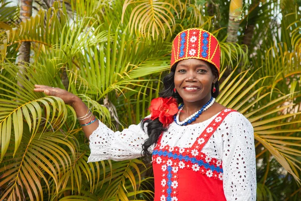 Bahçede güzel yeşil palmiye ağaçlarına karşı poz veren parlak renkli Rus elbiseli mutlu bir Afro-Amerikalı kadının portresi. Gelenekler, moda, dünya turizmi.