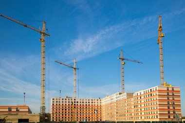 Açık bir günde mavi bulutlu gökyüzüne karşı konut binalarının inşaat vinçlerinin görüntüsü. İnşaat, yatırım, iş.
