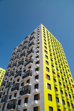 Sarı-yeşil renkli, turuncu eklemli, menteşeli balkonlu, dikey olarak çekilmiş güzel bir apartman manzarası. İş Finansmanı inşaat yatırımı.