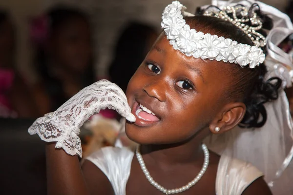Portrait of a cheerful little girl in a wedding dress, a hand in a white glove is near her mouth. Very cute kids in the Wedding Ceremony. Selective focus, children family happiness.