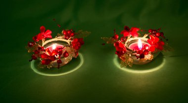 Yeşil arka planda parlak kırmızı çiçeklerle süslenmiş yanan mumlar. Deepavali ışık ve ateşi kutluyor. Dünya halklarının bayram gelenekleri..