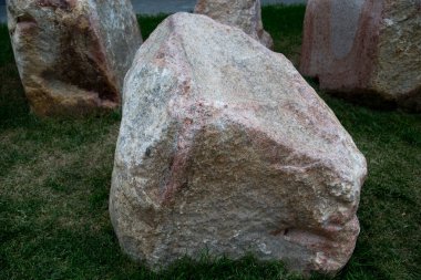 Taş yeşil çimlerin üzerindeki pembe granitten yapılmış bir kaldırım taşı. İnşaat malzemeleri, teknolojiler.