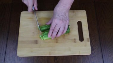 Salata için ahşap bir kesme tahtasının üzerinde elle salatalık kesiyor. Yiyecek ve içecekler