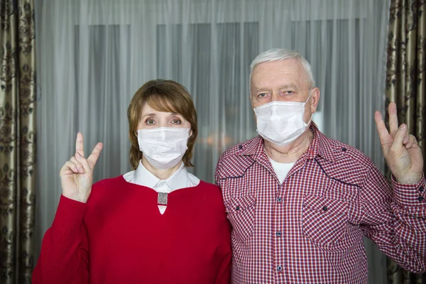 Beyaz maskeli, elleri ve parmakları havada, V harfini gösteren orta yaşlı bir kadın ve erkek yerleşim yerindeki bir binada zafer, viral enfeksiyondan korunma, grip, tüberküloz. İlaç, SARS 'tan koruma CoV-2 
