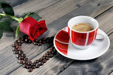 Eski ahşap bir masa üzerinde bir fincan kahve ile kırmızı bir ro süslenmiş görünümü