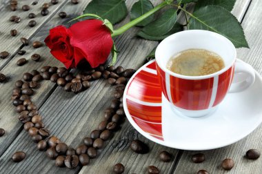 Eski ahşap bir masa üzerinde bir fincan kahve ile kırmızı bir ro süslenmiş görünümü