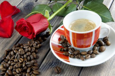Eski ahşap bir masa üzerinde bir fincan kahve ile kırmızı bir ro süslenmiş görünümü