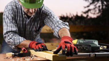 Adult carpenter craftsman wearing helmet and protective gloves, with a pencil and the carpenter's square trace the cutting line on a wooden table. Construction industry, housework do it yourself. Footage.