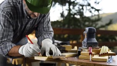 Adult carpenter craftsman wearing helmet and leather protective gloves, with a pencil and the carpenter's square trace the cutting line on a wooden table. Construction industry, housework do it yourself. Footage.