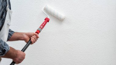 Beyaz tulumlu beyaz boyacı duvarı beyaz boyayla silindirle boyardı. İnşaat endüstrisi. İş güvenliği.