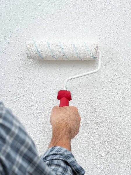 Caucasian house painter worker in white overalls, painting the wall with white paint using the roller. Construction industry. Work safety.