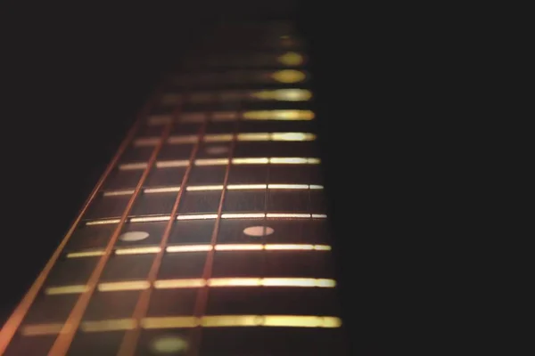 Closeup of guitar neck in vertical position with strings in copper colour on black background