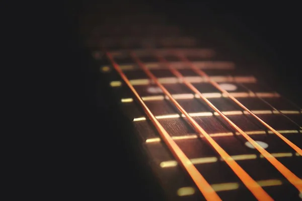 Closeup of guitar neck in diagonal position with strings in copper colour on black background