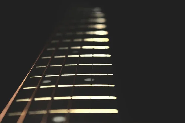 Closeup of guitar neck in vertical position with strings in silver colour on black background