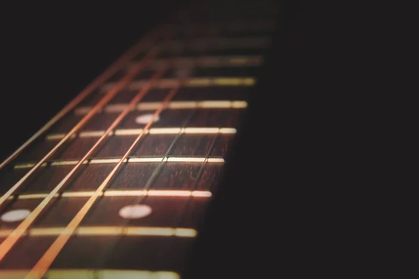 Closeup of guitar neck in diagonal position with strings in copper colour on black background