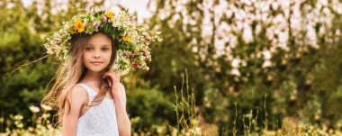 Çiçek çelengi takmış sevimli, gülümseyen küçük bir kız.