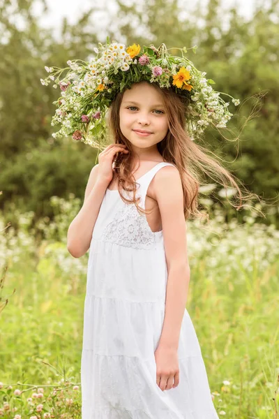 Roztomilé usmívající se holčička s květinovým věncem na louce v th — Stock fotografie