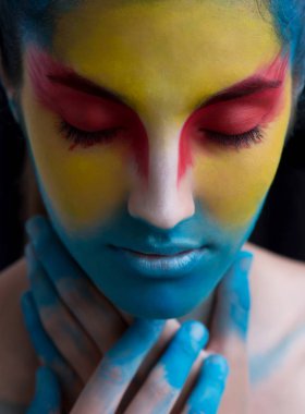Boyalı güzel kadın yüz, sanatsal makyaj, vücut ve yüz sanatı, yakın. Yüz ifadesi, duygular. Kırmızı, sarı, mavi renklerde Kuş Halloween güzellik moda tarzı. Halloween