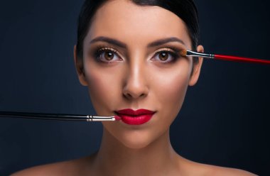 Parlak makyajlı ve iki kozmetik brolu güzel bir manken.