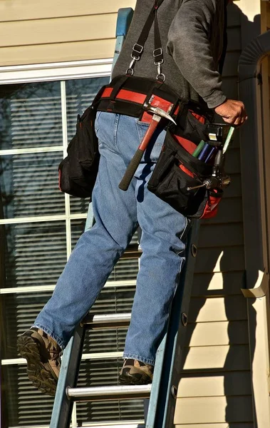 A construction repair worker leans on a ladder to make a repair,