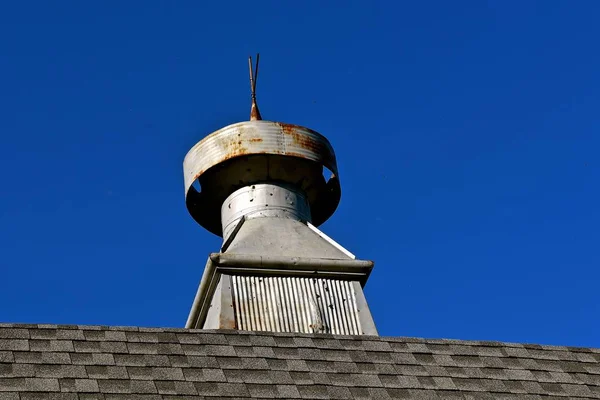 A metal cupola on the roof line of a shingled barn is riddled with bullet holes.