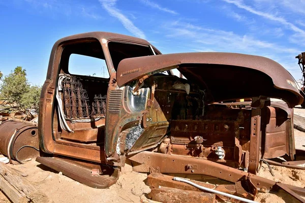 A side profile of a very old rusting truck missing the door and open hood exposing the engine