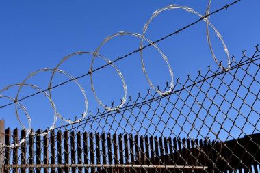 Razor sharp concertina wire on top of fences which provide a border between Mexico and the USA clipart