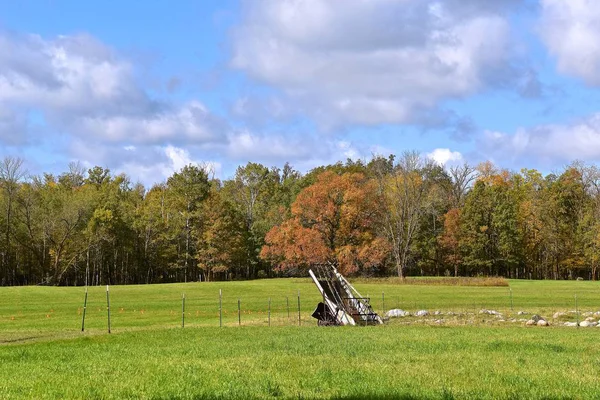 An old hay walker is left in a field with a background of trees in the early season of fall